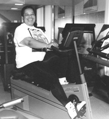 Photo of a very large woman smiling while peddling an exercise bike